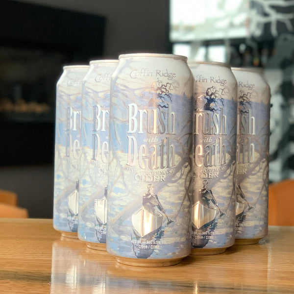 Six cans of  Brush With Death cider on a wooden table with a blurred indoor background